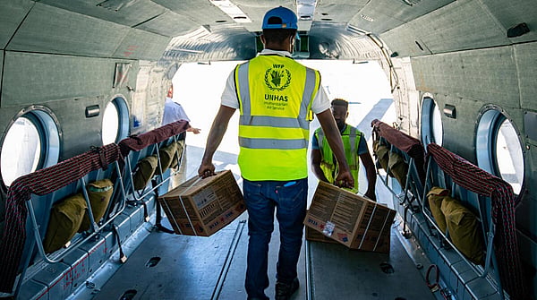 World Food Programme worker inside a cargo airplane holding boxes in both arms, surrounded by stacked boxes.